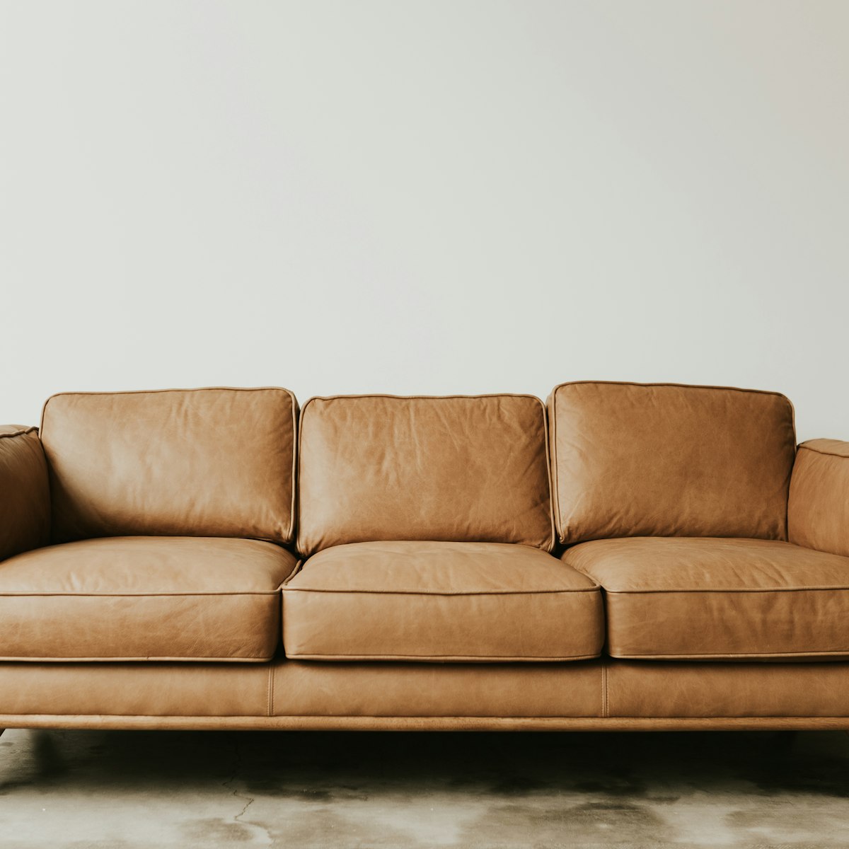 Tan leather three-seater sofa with tapered wooden legs